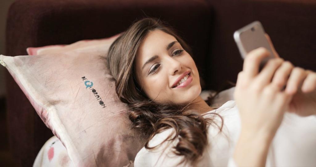 a woman on a sofa smile to her smartphone while using the Lexa dating app