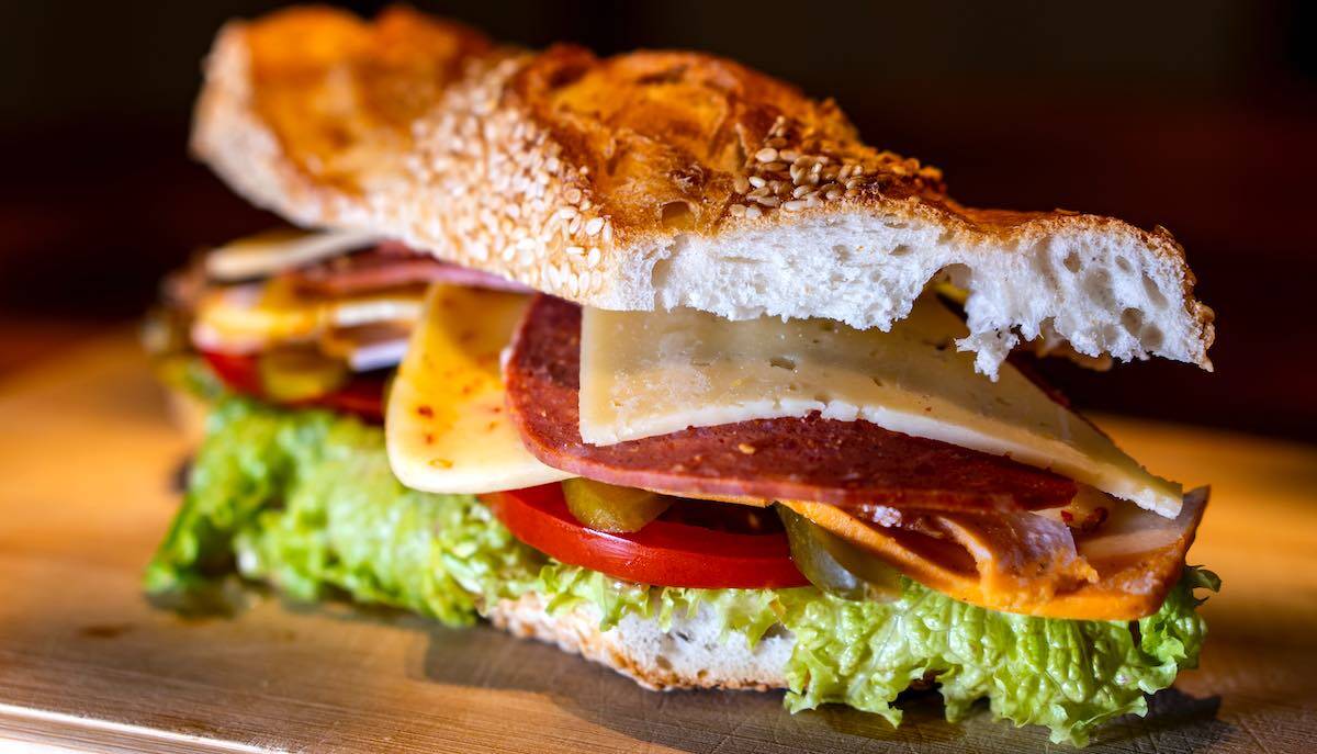 sandwich with cheese, salami, lettuce, tomato served on a wooden board.