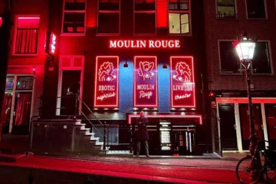 The front of Moulin Rouge Amsterdam in the Red Light District with a bouncer in front of it surrounded by red light neon.