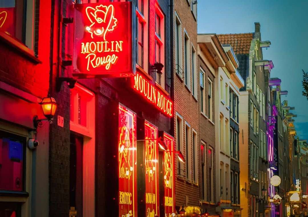 The logo of Amsterdam's Moulin Rouge at night with some canal house in the background
