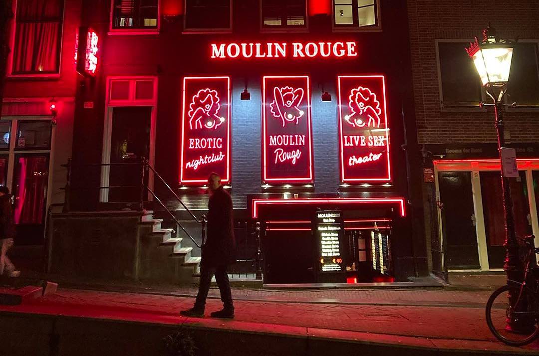 a man in front of Moulin Rouge in Amsterdam Red Light District with the logo of the venue in the background and white lantern on the right front