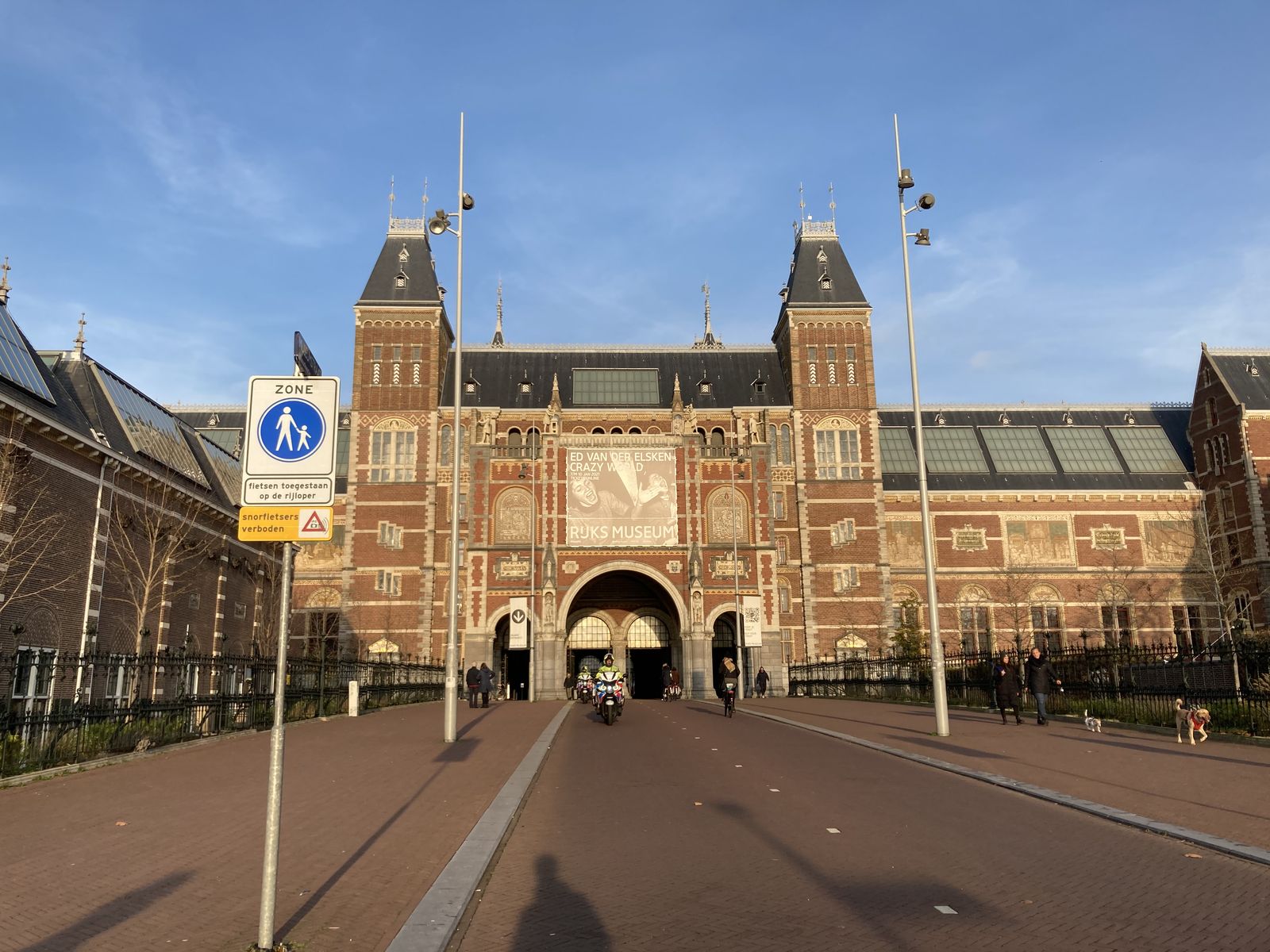 The red-brick facade of the Rijksmuseum in Amsterdam, seen from the museum square with cyclists passing under the central archway